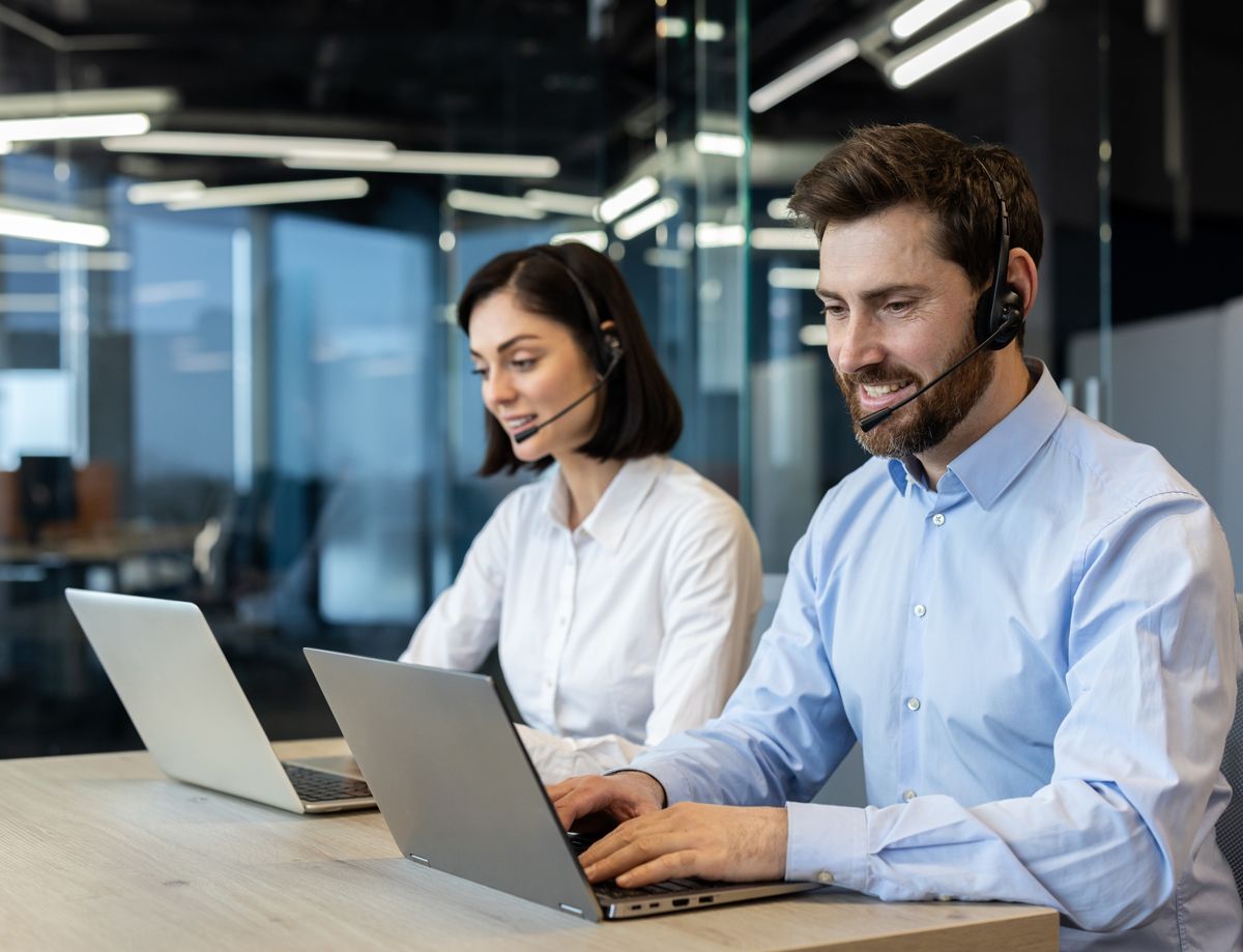 Dos empleados en un centro de atención al cliente trabajando en laptops.