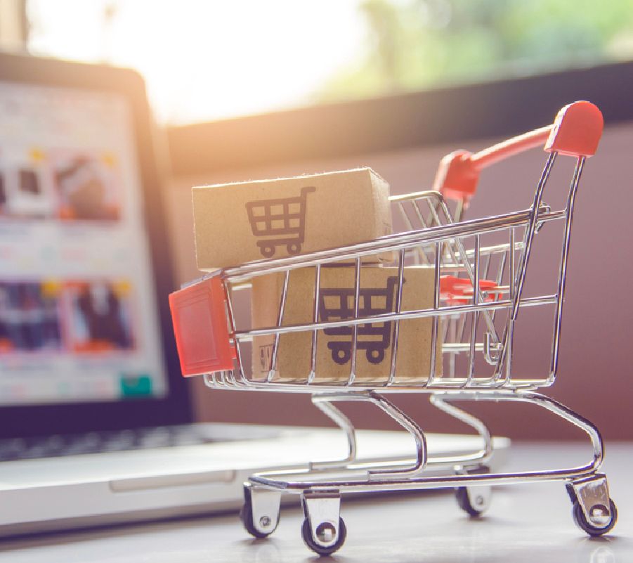 Carrito de compras pequeño frente a una laptop mostrando una tienda online.