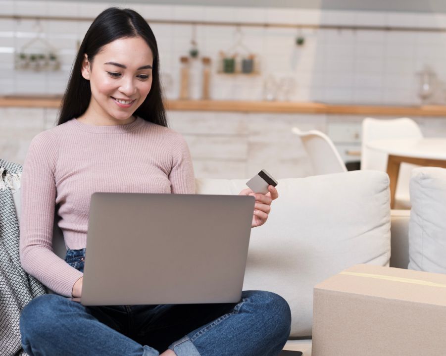 Mujer sonriente usando una laptop con una tarjeta de crédito en mano.